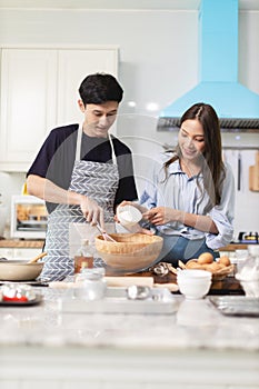 Asian couple Help each other to make a bakery In a romantic atmosphere in the kitchen at home. Young people work together to mix