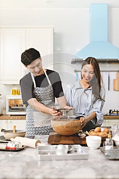 Asian couple Help each other to make a bakery In a romantic atmosphere in the kitchen at home. Young people work together to mix