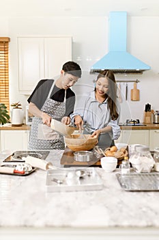Asian couple Help each other to make a bakery In a romantic atmosphere in the kitchen at home. Young people work together to mix