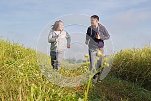 Asian couple jogging together, outdoor morning run in nature trail organic rice paddy field. Healthy lifestyles and sustainability