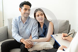 Asian couple join hand to encourage while sitting on the couch in the psychiatrist room to consult mental health problems by