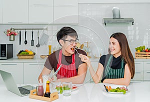 Asian couple in love is sitting in kitchan by woman is feeding sausage her man