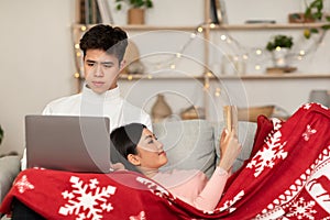 Couple Reading Book And Watching Movie On Laptop At Home