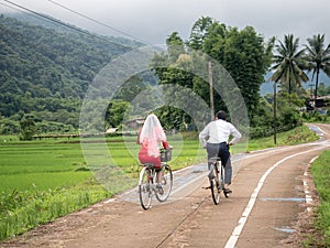 Asian couple riding bicycle on countryside road near rice field. wedding concept.