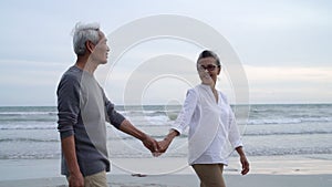 Asian couple senior elder retire resting relax holding hand walking at sunset beach