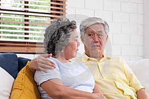 Asian couple senior embracing and sitting comfortably on sofa and  talking in living room at home photo