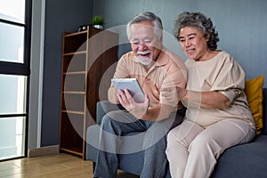 Asian couple of seniors smiling and looking at the same tablet on the sofa at home