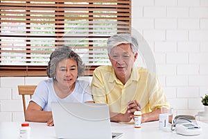 Asian couple seniors use laptop video conference with doctor about illness and prescription pill in living room at home.Healthy