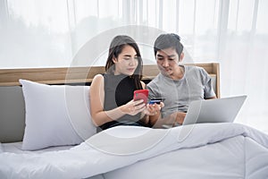 Asian Couple shopping online and paying with credit card on laptop and mobile phone at home,Happy couple at home surfing the net