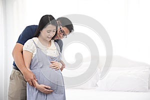 Asian couple sitting and embracing wife 8 months tummy.  Family waiting for newborn baby