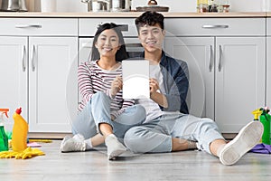 Asian couple sitting on floor at kicthen, showing digital tablet