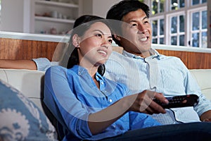 Asian Couple Sitting On Sofa Watching TV Together