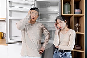 Asian couple standing by empty fridge at home