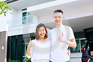 Asian couple standing in front of their new house and giving thumbs up