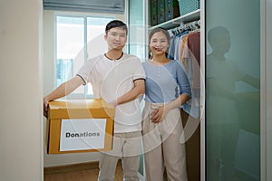 Asian couple are standing near closet of clothes in the dressing room carrying a box of clothes donated to take to the donation