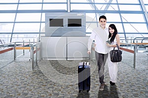 Asian couple with suitcase smiling in airport terminal
