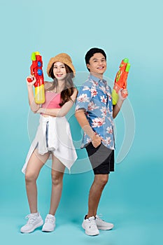 Asian couple in summer clothes with water gun in studio blue background. They smile and look at the camera at the Songkran