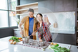 asian couple taking selfie while cooking together in the kitchen