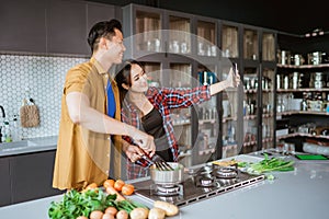 asian couple taking selfie while cooking together in the kitchen