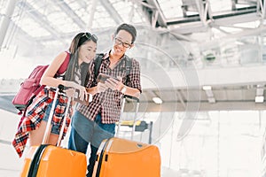 Asian couple travelers using smartphone checking flight or online check-in at airport, with passport and luggage