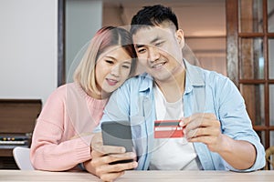 Asian couple use mobile phone shopping online with credit card together in living room at home.couple in home concept