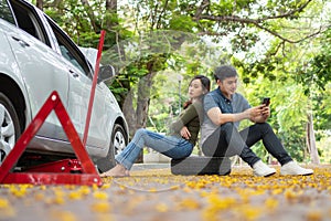 Asian couple using smartphone for assistance after a car breakdown on street. Concept of vehicle engine problem or accident and