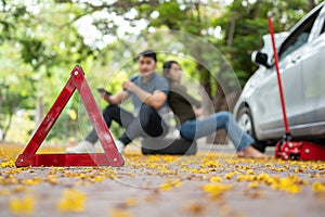 Asian couple using smartphone for assistance after a car breakdown on street. Concept of vehicle engine problem or accident and