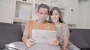 Asian couple using tablet for online shopping in internet in living room at home, sweet couple enjoy love moment.