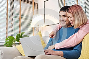 Asian couple watching video live on laptop on sofa in living room at home.lover spending time together.