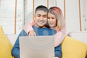 Asian couple watching video live on laptp on sofa in living room at home.lover spending time together.wife embrace husband from