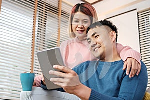 Asian couple watching video live on tablet on sofa in living room at home.lover spending time together.