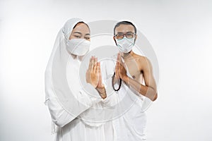 Asian couple wearing ihram clothes and mask with salam gesture