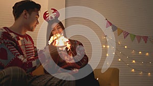 Asian couple wearing sweaters playing tangled led lights ball together on the sofa in the living room at home on Christmas eve