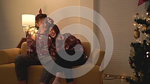 Asian couple wearing sweaters playing tangled led lights ball together on the sofa in the living room at home on Christmas eve