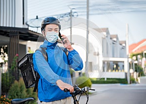 Asian courier man in uniform wear medical face mask, helmet using bicycle with backpack for food delivery of order to customer