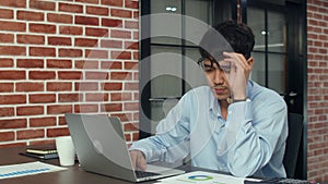 Asian creative man stress while working on laptop. Young professional business male using computer looking information paper,