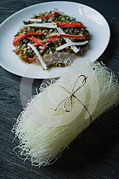 Asian cuisine. Raw cellophane noodles. In the background is decorated with cellophane noodles salad with vegetables, greens.