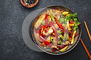 Asian cuisine, stir fry with chicken, red paprika pepper and zucchini bowl. Black kitchen table background, top view, copy space