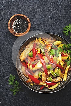 Asian cuisine, stir fry chicken, red paprika and zucchini with sesame and soy sauce in bowl. Black table background, top view,