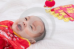 Asian cute baby boy Chinese Cheongsam costume toddler lie down on bed at home wiht gold ingots laughing good humored  infant