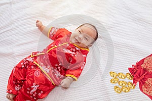 Asian cute baby boy Chinese Cheongsam costume toddler lie down on bed at home wiht gold ingots laughing good humored  infant