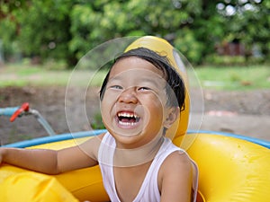 Asian cute child boy laughing while playing outdoor in yellow duck rubber band with rural nature background.