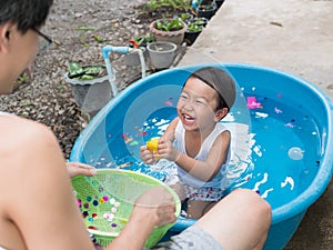 Asian cute child boy laughing while playing water in blue bowl with relaxing face and wet hair in rural nature.