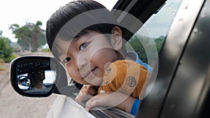 Asian cute child boy looking out car window with happy smiling face and hugging teddy bear with love.