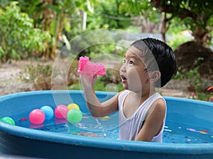 Asian cute child boy playing water in blue bowl with relaxing face and wet hair in rural nature.