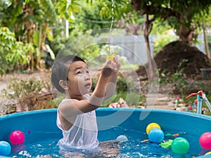 Asian cute child boy playing water in blue bowl with relaxing face and wet hair in rural nature.