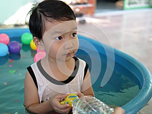 Asian cute child boy  playing water in blue bowl with relaxing face and wet hair. Young kid having happy moment in summer.