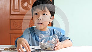 Asian cute child holding transparent piggy bank and looking with surprised face at home.