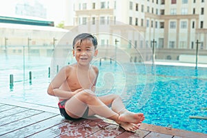 Asian cute child swimming in swimming pool. He playing is funny on summer holiday on blurred background. Cute boy smile and swim