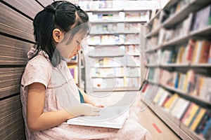 Asian cute girl 6-7 years reading a book in public library